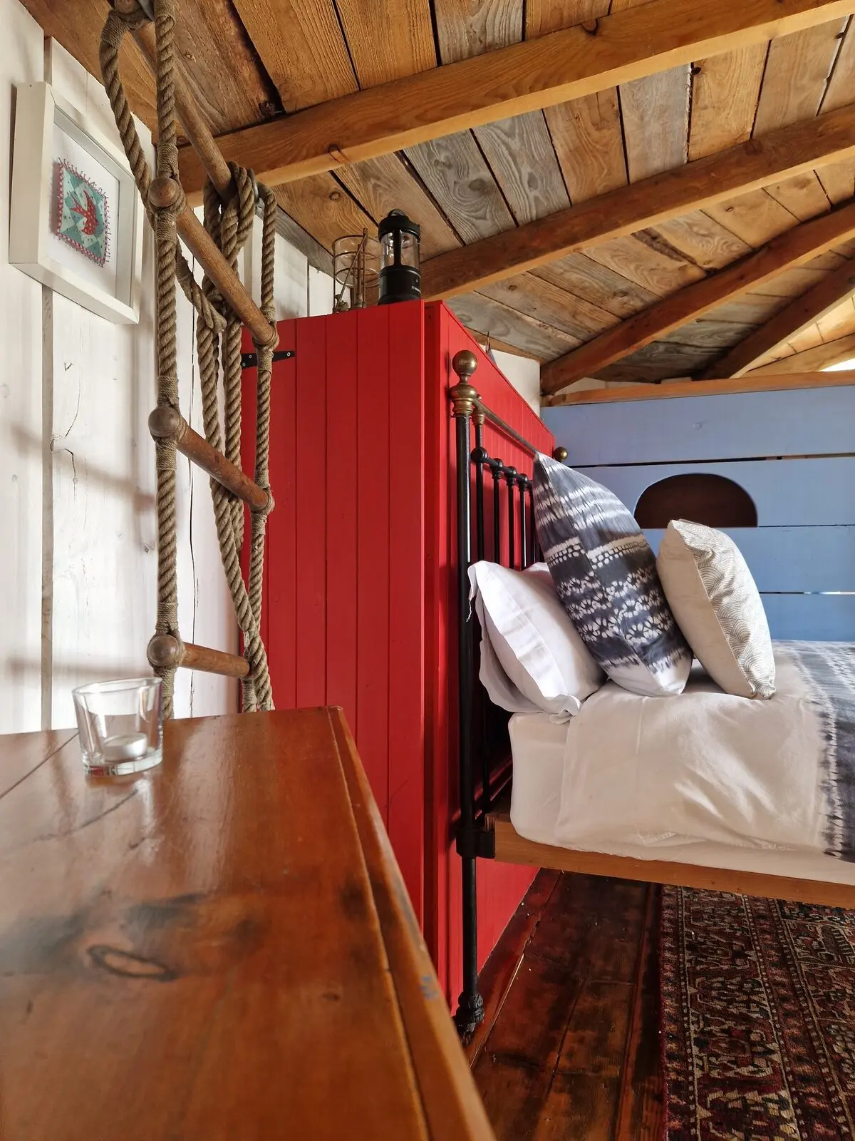 The red partition and iron bed frame with cushions, rope railing, and lantern under the timber ceiling