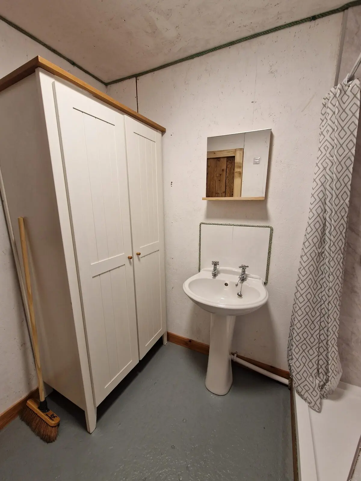 Inside the shower room — wardrobe, pedestal basin, mirror, and patterned shower curtain