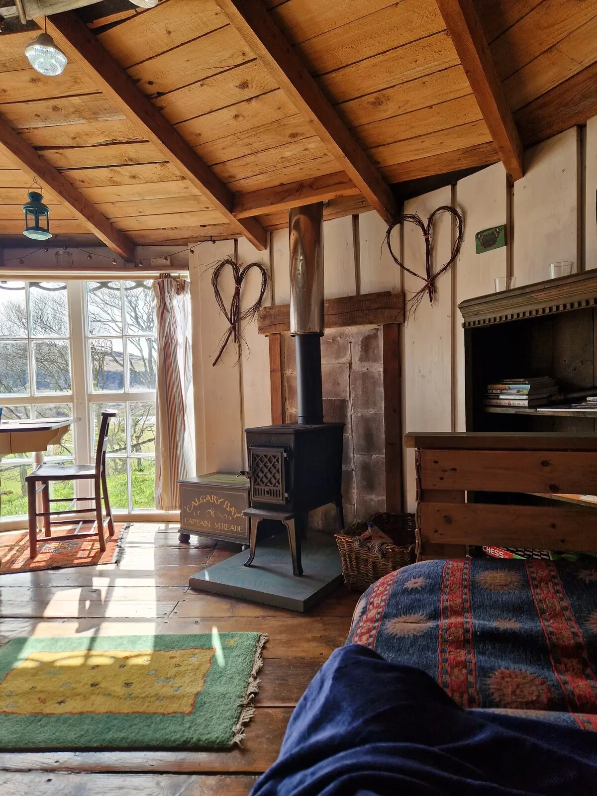The wood-burning stove and heart decorations seen from the sofa, with sunlight through the bay windows beyond
